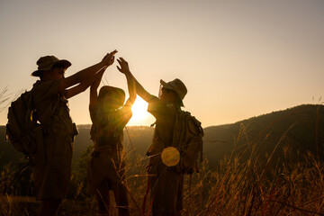 Three Boy Scouts in camp with backpacks holding hands on the mountain Boy Scouts rejoice at rock climbing success in the evening at sunset. - obrazy, fototapety, plakaty