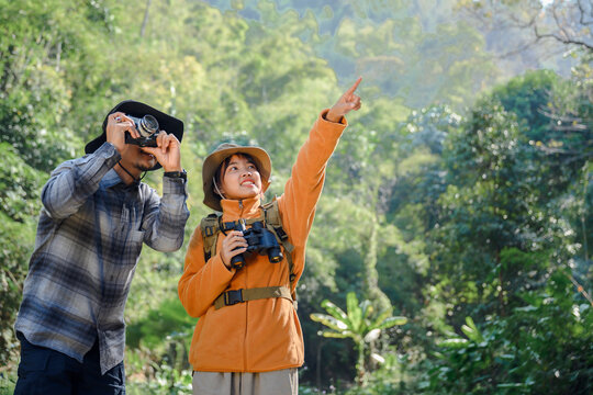 Asian female backpacker talking to male tourist Take pictures with a camera while hiking explore nature in the forest Happy enjoying the trekking through nature.