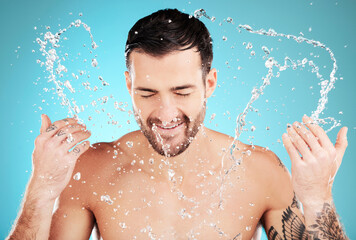 Water, skincare and man with facial splash, smile and morning cleaning treatment isolated on blue background. Face, hygiene and male model grooming for health, wellness and clean skin care in studio.
