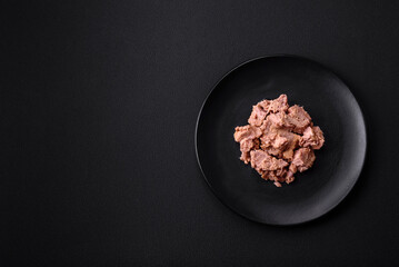 Delicious canned tuna meat on a black ceramic plate on a dark concrete background