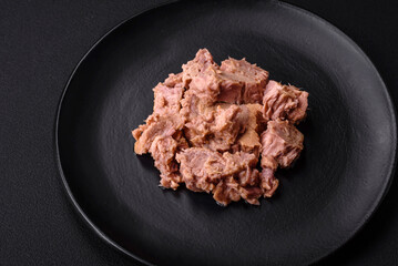 Delicious canned tuna meat on a black ceramic plate on a dark concrete background