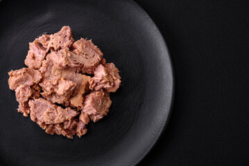 Delicious canned tuna meat on a black ceramic plate on a dark concrete background
