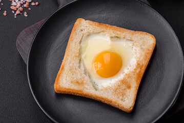 Heart shaped fried egg in bread toast with sesame seeds, flax seeds and pumpkin seeds on a black plate