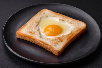 Heart shaped fried egg in bread toast with sesame seeds, flax seeds and pumpkin seeds on a black plate