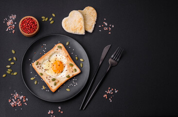 Heart shaped fried egg in bread toast with sesame seeds, flax seeds and pumpkin seeds on a black plate