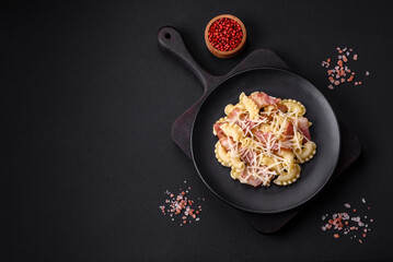 Delicious pasta with bacon and parmesan cheese on a black ceramic plate