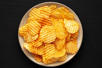 Barbeque Potato Chips on a plate on a black background, top view. Flat lay, overhead, from above.