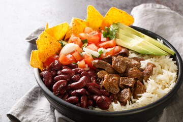 Chifrijo is a delicious traditional Costa Rican dish made with red beans and pork, accompanied by pico de gallo and rice closeup on the plate on the table. Horizontal