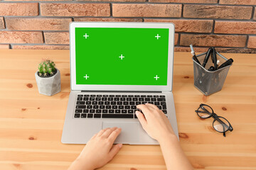 Young woman using laptop at wooden desk, closeup. Device display with chroma key