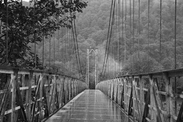 Metal bridge over river in mountains, toned in black and white