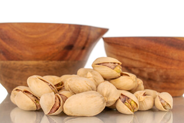 Several unshelled pistachios with two wooden cups, close-up, isolated on white.
