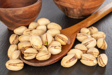A few unshelled pistachios with a wooden spoon on a slate stone, close-up.