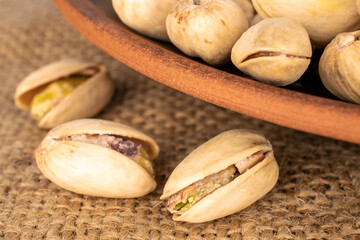 A few unshelled pistachios in a clay plate on a jute cloth, close-up.