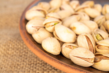 A few unshelled pistachios in a clay plate on a jute cloth, close-up.