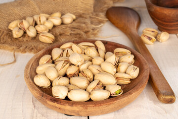 A few unshelled pistachios in a white ceramic plate on a wooden table, close-up.