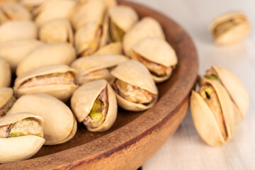 A few unshelled pistachios in a white ceramic plate on a wooden table, close-up.
