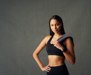 Young biracial woman wearing sports bra and fitness tracker holding towel over shoulder in studio