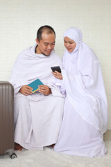Obraz na płótnie Canvas Muslim couple hajj or umrah wearing islamic white ihram while using smartphone