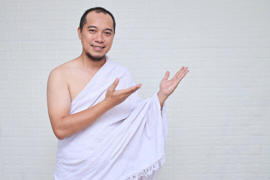 Asian muslim man wearing white ihram clothes pointing something to the side, copy space for advertisement