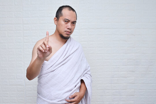 Asian muslim man wearing white ihram clothes and showing index finger means stopping you, say no or don't.
