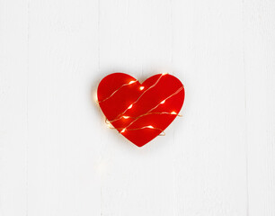Valentine's Day concept. Red heart with the light string on the white wooden background.
