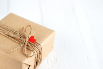 Gift box of craft paper with hearts on the white wooden background. Valentine's Day.