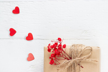  Valentine's Day flatlay. Gift box of craft paper with hearts and red flowers on the white wooden background.