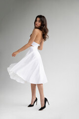 Full length image of young woman with hairstyle and makeup in sensual white dress posing in studio, it spins.