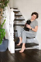 Woman sitting on stairs, using smartphone with black griffon or pug on her lap