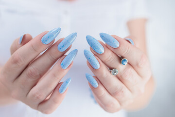 Female hand with long nails and light blue manicure with bottles of nail polish