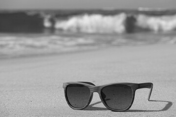 Monotone sunglasses on the sandy beach with blurry splashing waves in background