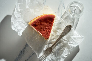 A piece of Basque cheesecake on parchment with a fork. Sunlight in the morning. Minimalist concept with space for text