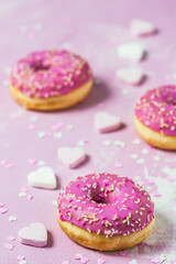 Donuts, Berliner, Krapfen with pink sugar icing on pink textured background, decorated with pink and white sugar and paper hearts, vertical