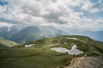 Fototapeta premium mountain landscape with clouds, lake and people hiking