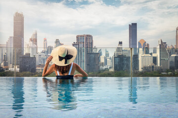 A woman with hat enjoys the elevated view over the urban skyline of Bangkok, Thailand, from a swimming pool