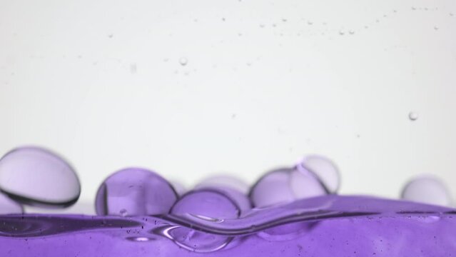 Background shot for cosmetics with bakuchiol commercial | Macro shot of a lot of different sized purple clear bubbles fall down to purple surface bouncing and bursting on grey background
