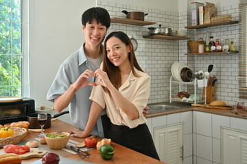 Happy loving couple making heart shape with their hands and smiling to camera, enjoying leisure time at home