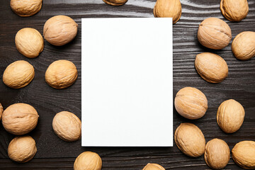 Blank card mockup with walnut shells on wooden background, top view, flat lay. White holiday card on brown table