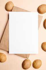 Blank card mockup with walnut shells and envelop on beige background, top view, flat lay. White...