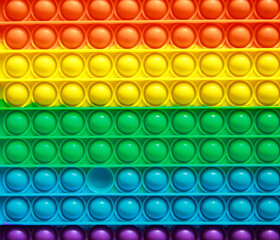 Bright, developing popular anti-stress toy. Colorful fashion anti-stress sensory toys fidget push pop it. Bright rainbow background. Autism and Down syndrome.