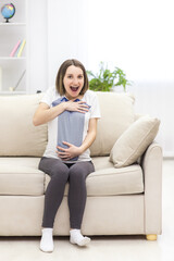 Photo of pregnant woman wearing casual clothes and holding childish clothes in hands.