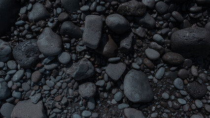 Beautiful dark texture of stones on the ocean beach, top view. Rocky beach on the volcanic island of Madeira