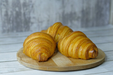Fresh baked croissants on wooden cutting board on concrete grey surface in dark 