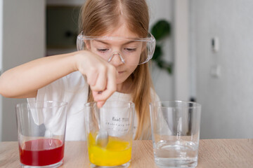 child learning research and doing a chemical experiment while making analyzing and mixing liquid in test glasses. Playful little girl in protective wear having fun playing with chemistry lab game. 