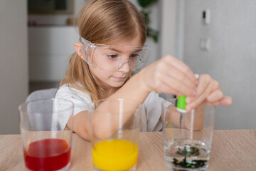 child learning research and doing a chemical experiment while making analyzing and mixing liquid in test glasses. Playful little girl in protective wear having fun playing with chemistry lab game. 