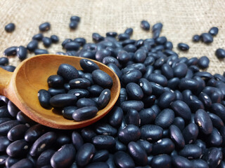 Black beans on wooden spoon isolated on sackcloth background. raw beans and organic superfood