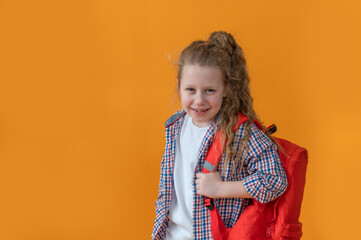 cute joyful girl child 6-7 years old on an isolated yellow background in with a school backpack adjusts glasses. High quality photo	