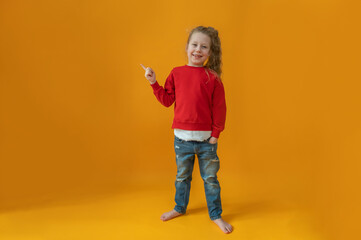 cute joyful baby girl in a red sweater with a red heart in her hands on an isolated yellow background valentine's day concept. High quality photo