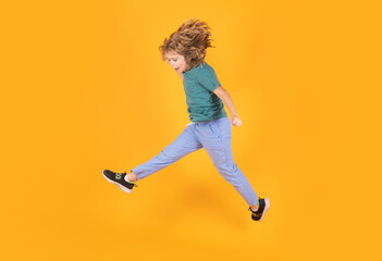 Child boy jump fly movement wear shirt and jeans isolated on yellow studio background.