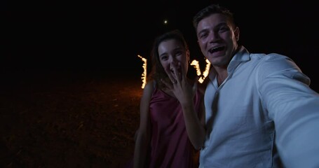 POV: Man and Woman Making Video Call to Friends and Family to Announce Their Engagement, With the Word LOVE Burning with fire letters in the Background. Happy Couple Sharing their Big Moment